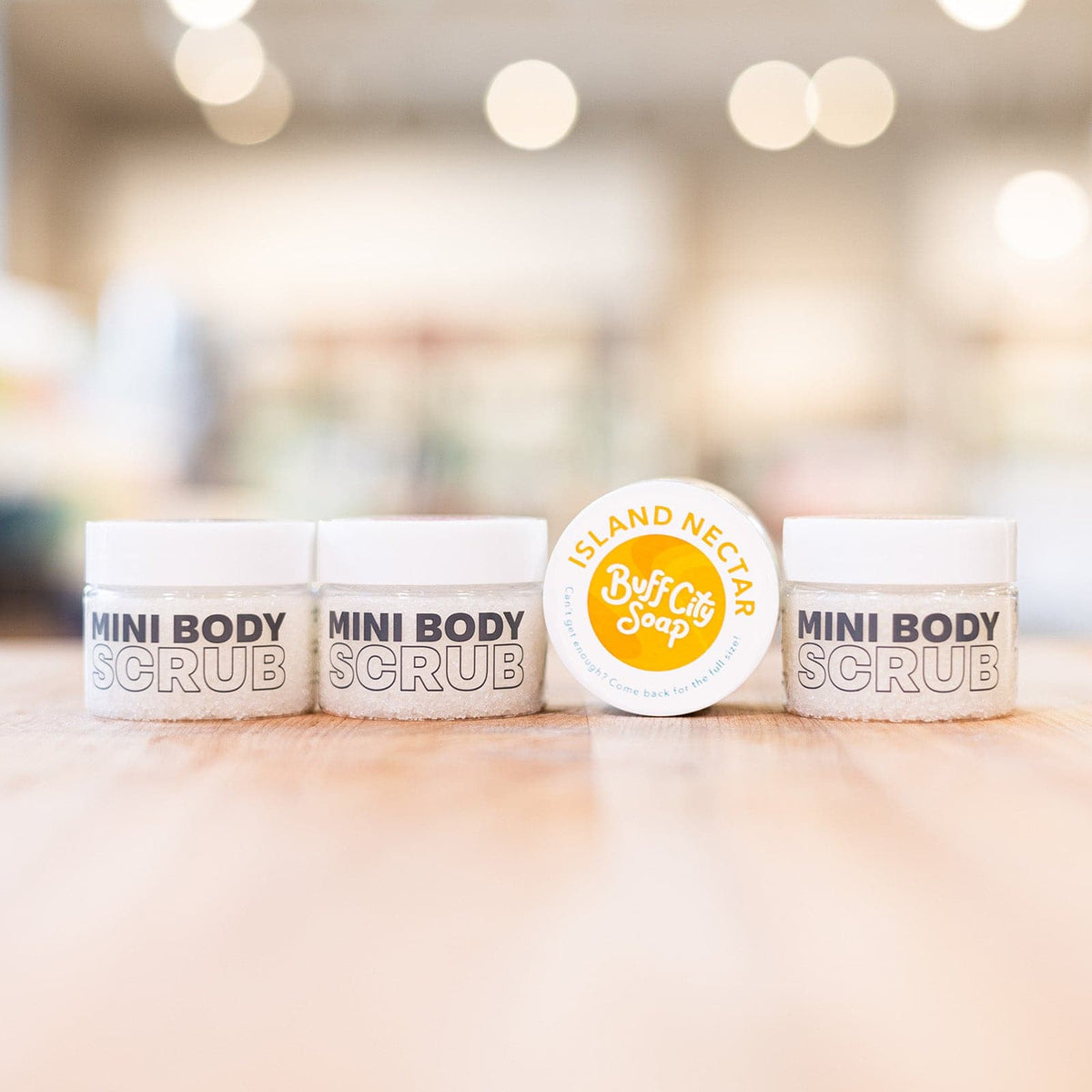 Four Mini Island Nectar Body Scrubs in containers lined up on counter
