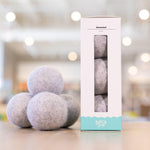 Three gray Unscented Dryer Balls placed next to a box of three Unscented Dryer Balls